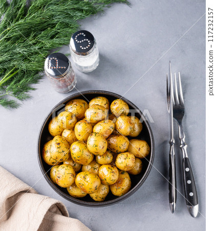 Young roasted baby potatoes in a black pan with salt and herb on a blue background. Young roasted baby potatoes in a black pan with salt and herb on a blue background. 117232157