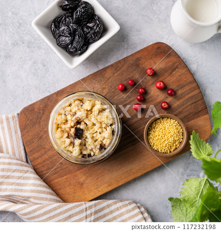 Millet porridge with prunes and fresh berry in a jar on a light background. Millet porridge with prunes and fresh berry in a jar on a light background. 117232198