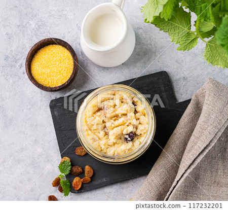 Corn porridge with rasin in a bowl on a blue background with milk. Concept of a healthy breakfast.  117232201