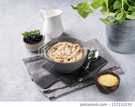 Millet porridge with prunes in a bowl on a blue background with milk. Millet porridge with prunes in a bowl on a blue background with milk. 117232210