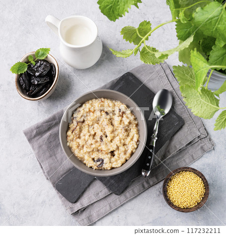 Couscous or millet  porridge with prunes in bowl  with milk on a blue background.  117232211