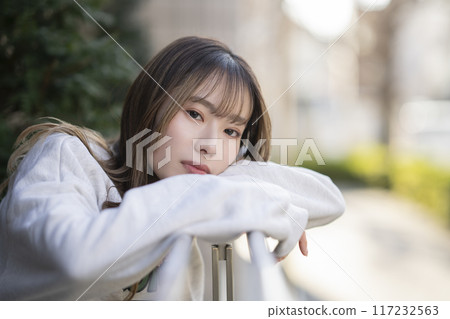 Woman in her 20s leaning on the railing of a terrace, looking at the camera, portrait Woman in her 20s leaning on the railing of a terrace, looking at the camera, portrait 117232563