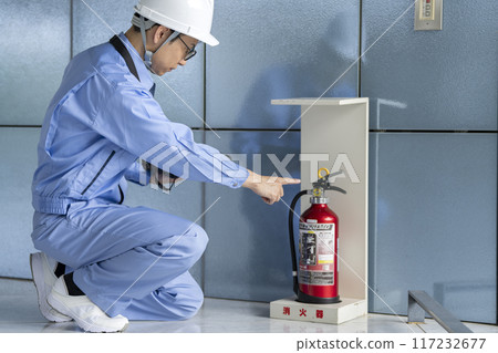 一名穿著工作服的男子檢查滅火器，建築物維護圖像 117232677