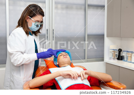 Skin lesion removal procedure. Dermatologist carrying out a removal of benign skin lesion on the face of a young male patient. 117234926