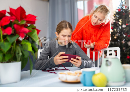 Mother is unhappy with daughter while daughter plays on smartphone Mother is unhappy with daughter while daughter plays on smartphone 117235785