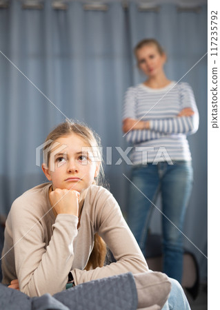 Sad female and daughter sitting at sofa and having quarrel 117235792