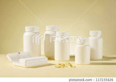 Several white mockup bottle without label neatly arranged on the table and featured on light yellow background, with a white pill box and some soft yellow supplement capsule flat lay on the table Several white mockup bottle without label neatly arranged on the table and featured on light yellow background, with a white pill box and some soft yellow supplement capsule flat lay on the table 117235826