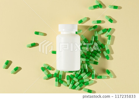 The promotional photo with a mockup medicine bottle featured above a layer of green pill capsules. Top shot, space for adding text and design elements 117235833