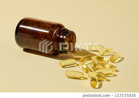 Pharmaceutical advertising mockup from front close up shot, an amber supplement jar without label flat lay on yellow surface with plenty scattered yellow supplement capsules by side. Copy space 117235838