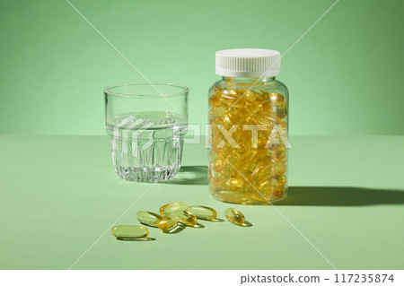 Template photo for nutritional supplement, clear jar of yellow capsules without label, next to a water glass and some flat lay vitamin supplements in front. Green background, blank space for designing Template photo for nutritional supplement, clear jar of yellow capsules without label, next to a water glass and some flat lay vitamin supplements in front. Green background, blank space for designing 117235874
