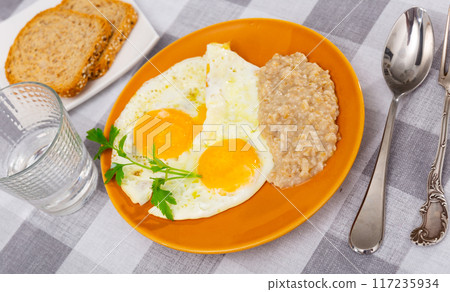 Portion of diet food on plate - two fried eggs and boiled oatmeal porridge 117235934