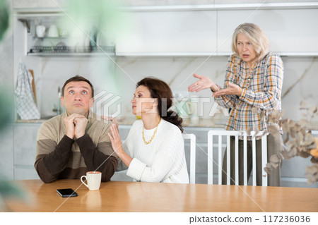 Family members quarreling in the kitchen and middle-aged woman trying to calm angry man Family members quarreling in the kitchen and middle-aged woman trying to calm angry man 117236036