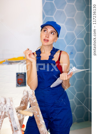 Woman foreman checks the completed construction work on drawing 117236130