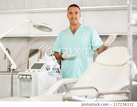 Portrait of male doctor cosmetologist wearing overall showing equipment of clinic before procedure 117236132