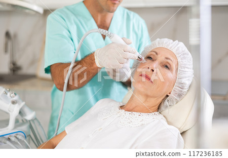 Male dermatologist performing cosmetology procedure for elderly woman, RF lifting and deep hydration for facial skin therapy Male dermatologist performing cosmetology procedure for elderly woman, RF lifting and deep hydration for facial skin therapy 117236185