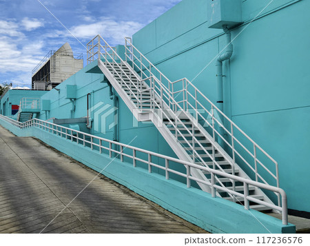 Metal stairs to blue building against sky and clouds Metal stairs to blue building against sky and clouds 117236576
