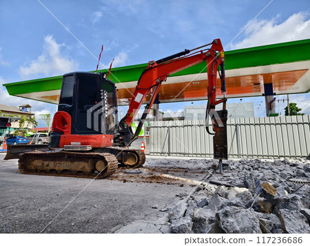 Excavator using hydraulic hammer for breaking concrete at a construction site Excavator using hydraulic hammer for breaking concrete at a construction site 117236686