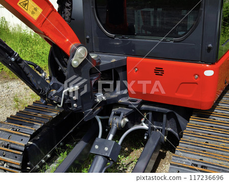 Red large excavators are stationed in a green field in front of a building Red large excavators are stationed in a green field in front of a building 117236696