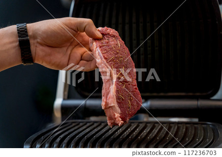 Chef at the kitchen preparing beef steaks on the home electric grill 117236703