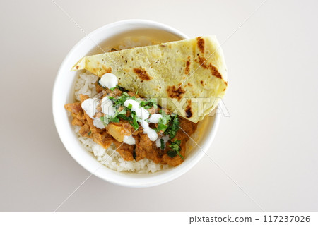 A bowl of chicken tikka masala w slice of naan bread and yogurt on a plate. 117237026