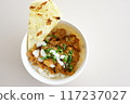 A bowl of chicken tikka masala w slice of naan bread and yogurt on a plate. 117237027