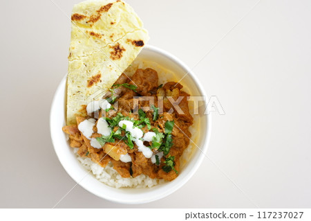 A bowl of chicken tikka masala w slice of naan bread and yogurt on a plate. 117237027