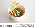 A bowl of chicken tikka masala w slice of naan bread and yogurt on a plate. 117237028