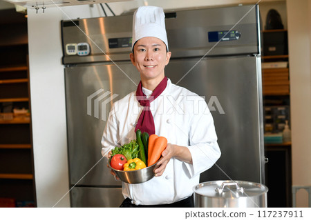 Young asian male chef holding lots of vegetables Young asian male chef holding lots of vegetables 117237911