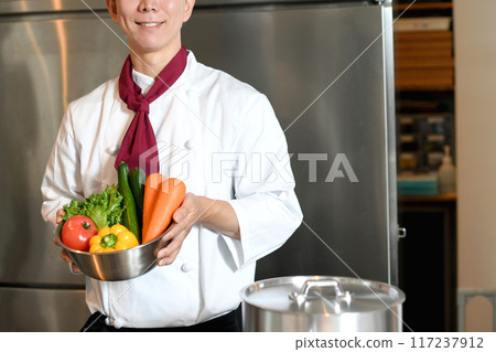 Young asian male chef holding lots of vegetables Young asian male chef holding lots of vegetables 117237912