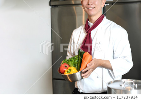 Young asian male chef holding lots of vegetables Young asian male chef holding lots of vegetables 117237914