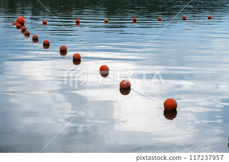 Orange buoys floating on calm water surface reflecting the sky. Orange buoys floating on calm water surface reflecting the sky. 117237957
