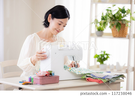 Hobby: Middle-aged woman sewing with a sewing machine Hobby: Middle-aged woman sewing with a sewing machine 117238046
