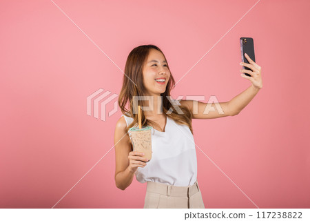 Asian woman takes photo of herself with drinking brown sugar flavored tapioca pearl bubble milk tea, smile female making selfie, studio isolated on pink background, pearl milk tea beverage concept 117238822