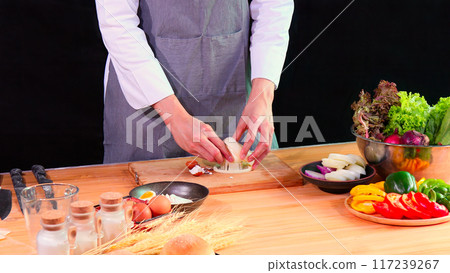 Young Chef using slicer cutting boiled egg on cutting board with fresh vegetables, ingredient, and spices on kitchen counter Young Chef using slicer cutting boiled egg on cutting board with fresh vegetables, ingredient, and spices on kitchen counter 117239267