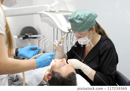 Dentist Closeup woman patient. Carious tooth treatment at dental clinic office. Nurse, doctor hand. Dentist making teeth cleaning, treating and canal filling. assistant spaying mouth Dentist Closeup woman patient. Carious tooth treatment at dental clinic office. Nurse, doctor hand. Dentist making teeth cleaning, treating and canal filling. assistant spaying mouth 117239369