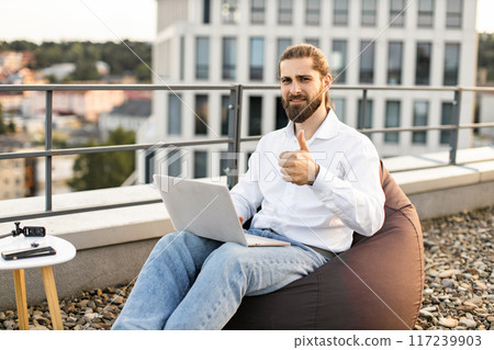 Freelancer working on laptop giving thumbs up on rooftop Freelancer working on laptop giving thumbs up on rooftop 117239903