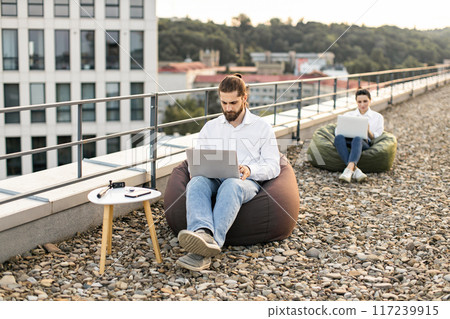 People working on laptops outside on rooftop with bean bags 117239915