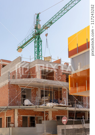 Vivid capture of construction site showcasing building in progress with brickwork and crane lifting materials. Ideal for real estate, development projects, and construction industry themes. Vivid capture of construction site showcasing building in progress with brickwork and crane lifting materials. Ideal for real estate, development projects, and construction industry themes. 117243282