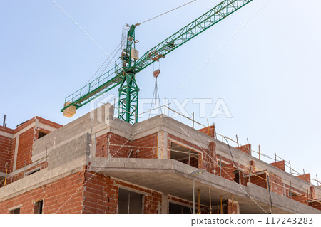 Vivid capture of construction site showcasing building in progress with brickwork and crane lifting materials. Ideal for real estate, development projects, and construction industry themes. Vivid capture of construction site showcasing building in progress with brickwork and crane lifting materials. Ideal for real estate, development projects, and construction industry themes. 117243283