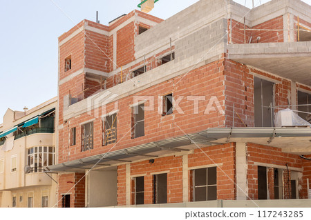 Close-up of an urban construction site with unfinished brick and concrete building under clear skies. Perfect for content related to urban development, architecture, and construction. 117243285