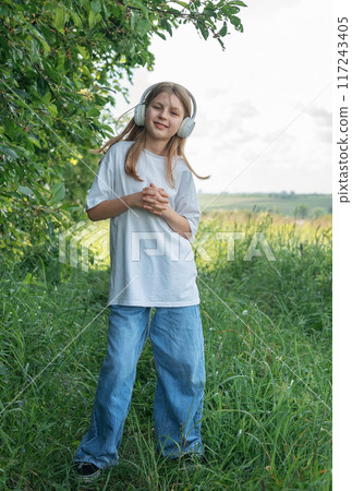 A child with headphones listening to music and dancing in the park.. A child with headphones listening to music and dancing in the park.. 117243405