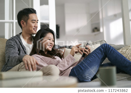 happy young asian couple looking at cellphone pictures together at home 117243862