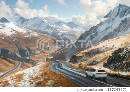 A car travels down a winding road surrounded by stunning mountains and colorful autumn scenery under a bright sky. 117245371