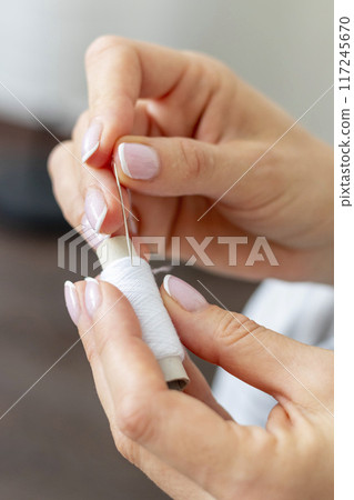 Shot of the woman with beautiful hands stitching up or patching a linen fabric 117245670