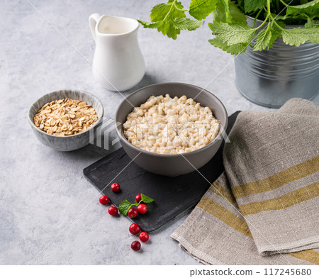 Oatmeal porridge with cranberry in bowl  with milk and oats flakes on a light background.  117245680