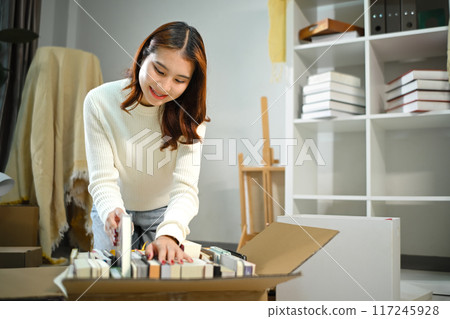 Smiling asian woman moving into new home, unpacking parcel box on floor in living room Smiling asian woman moving into new home, unpacking parcel box on floor in living room 117245928