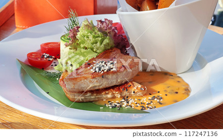 Grilled tuna with fresh vegetables and sauce, roasted potatoes. Food and dishes in restaurant. Useful and colorful food. Grilled tuna with fresh vegetables and sauce, roasted potatoes. Food and dishes in restaurant. Useful and colorful food. 117247136