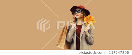 Autumn portrait, beautiful elegant happy woman with shopping bag holding yellow maple leaves in hat 117247206
