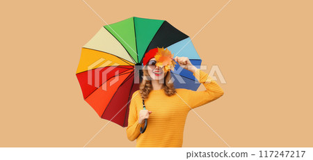 Autumn stylish cheerful young woman holds yellow maple leaves with colorful umbrella yellow sweater 117247217