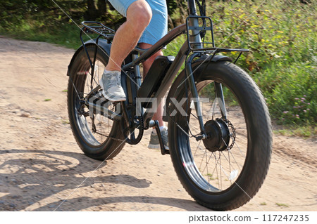 Cyclist on electric bicycle riding along path in field in countryside at sunset close-up. Sport and health. Summer hobby. Cyclist on electric bicycle riding along path in field in countryside at sunset close-up. Sport and health. Summer hobby. 117247235